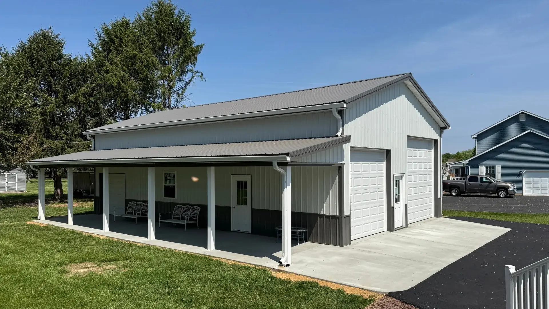 White Titan pole building with two garage doors and a full-length covered porch
